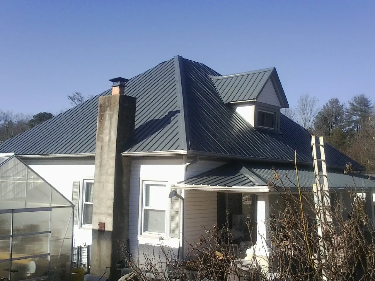 Dark blue standing seam metal roof on a white farmhouse with dormer — Slate & Tile Roof Repair by Roofing Brothers in Pine Lake