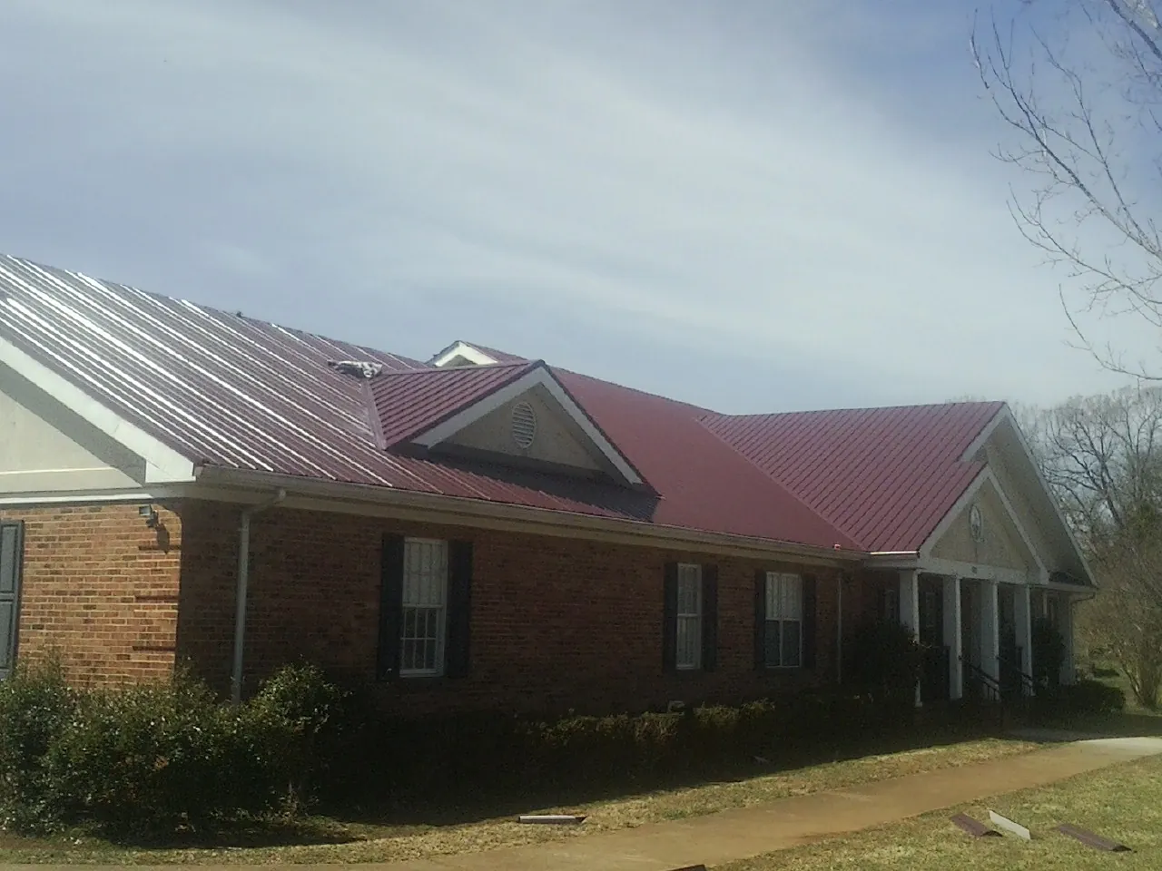 Red metal roof with gabled entries on a long brick building, from a Hail Damage Roof Repair job in Pine Lake
