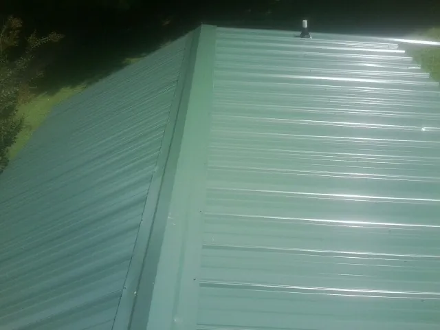 New green metal panels meeting at the ridge of a roof — Flat Roof Repair work by our crew in Pine Lake