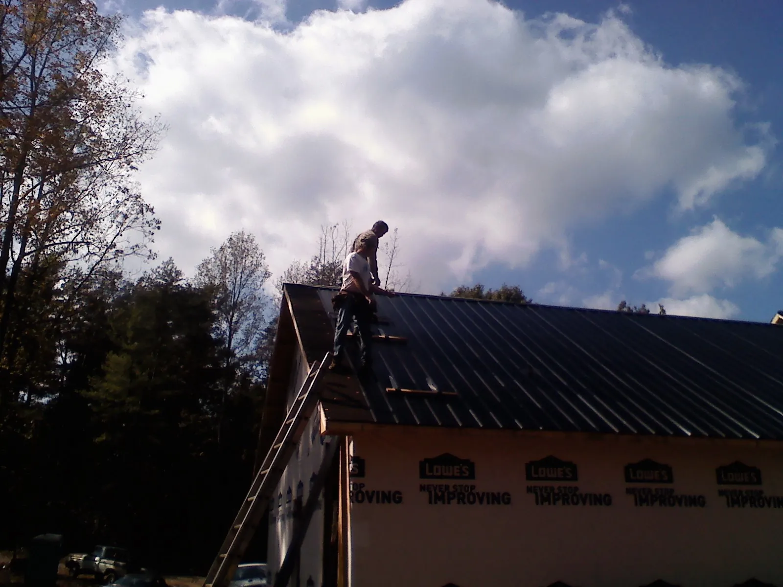 Roofer fastening dark metal panels high against a cloudy sky, from a Roof Inspection job in Pine Lake