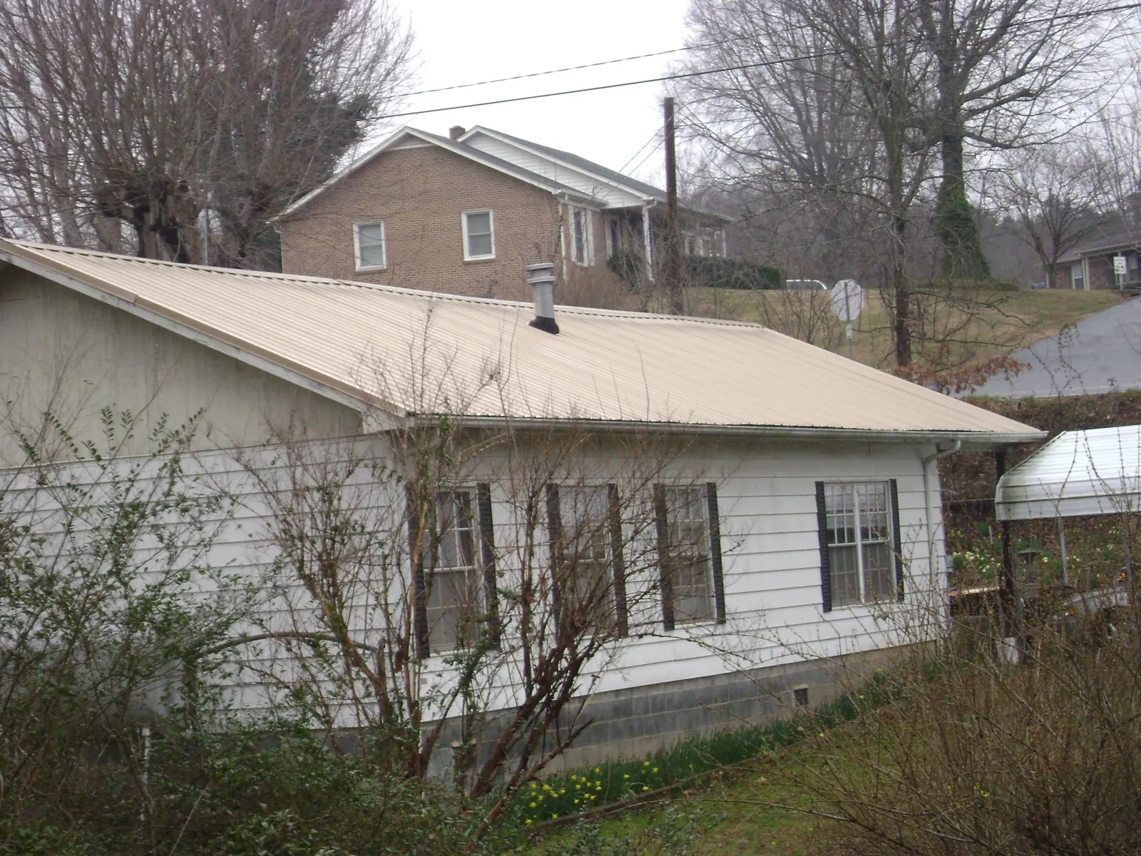 Tan metal roof on a white sided house set into a hillside — Commercial Roofing by Roofing Brothers in Pine Lake